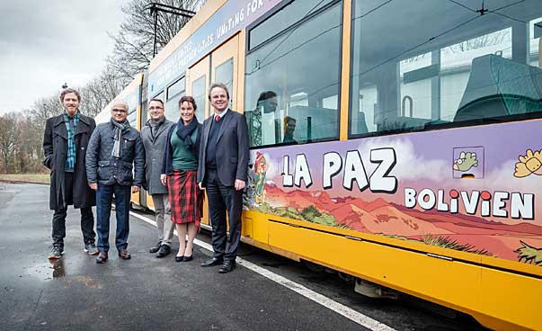Five people stand to the left of a colorfully illustrated tram.