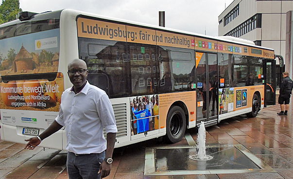 A man is standing in front of a bus, which is printed with different pictures and texts.