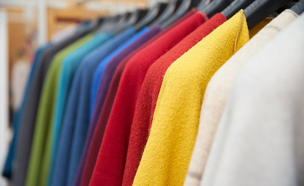 Jacken in den Farben weiß, rot, gelb, blau und grün hängen auf einer Kleiderstange.