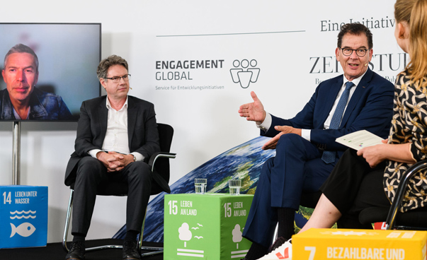 Bundesminister Dr. Gerd Müller diskutiert mit Christoph Heinrich (WWF) über das SDG 15. Zu sehen sind auch die Moderatorin rechts und eine weitere Person auf einem Bildschirm.