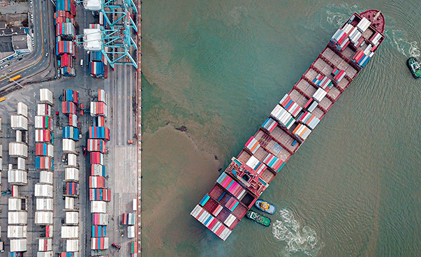Ein mit Containern beladenes Schiff liegt vor einem Containerhafen