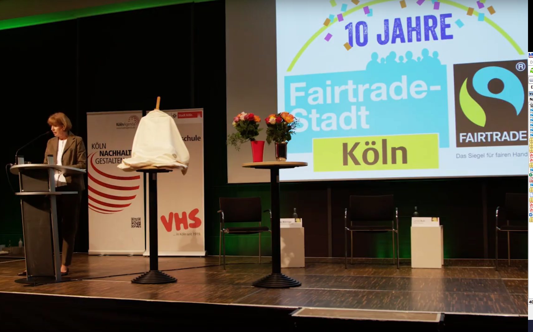 Eine Person spricht auf einer Bühne; rechts ist eingroßes Fair Trade-Logo zu sehen.