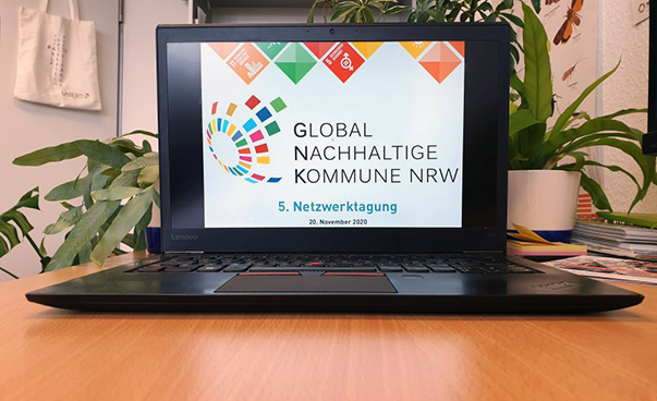 Auf dem Bildschirm eines auf einem Holztisch stehenden Laptops ist das GNK-NRW-Logo und der Zusatz Fünfte Netzwerktagung zu sehen.