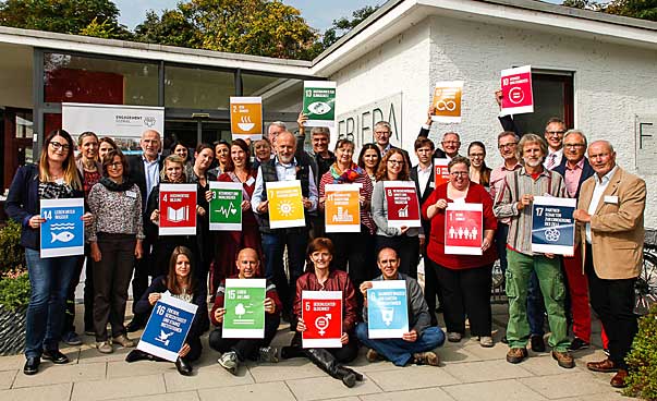 A group smiles at the camera, some of the people carry signs with the symbols of the 17 sustainable development targets.