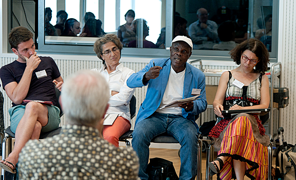 Eine Gruppe von fünf Personen sitz in einer Runde zusammen und hört einem Mann zu, der spricht. Foto: Jo Hempel