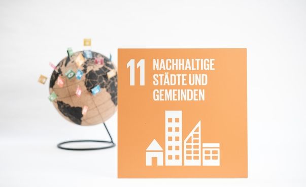 Das Symbol des globalen Nachhaltigkeitsziels 11 (Nachhaltige Städte und Gemeinden) mit einem Globus im Hintergrund.