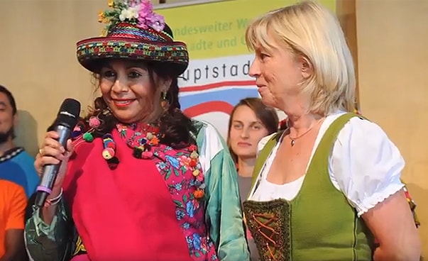 Zwei Frauen stehen nebeneinander; eine trägt ein Dirndl, die andere eine südamerikanische Tracht.