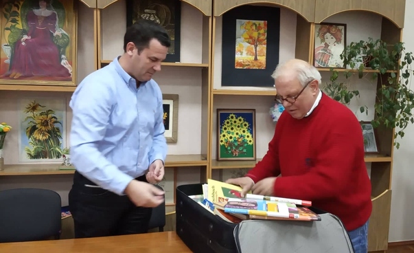Zwei Männer in einer Bibliothek schauen in einen geöffneten Koffer mit Büchern