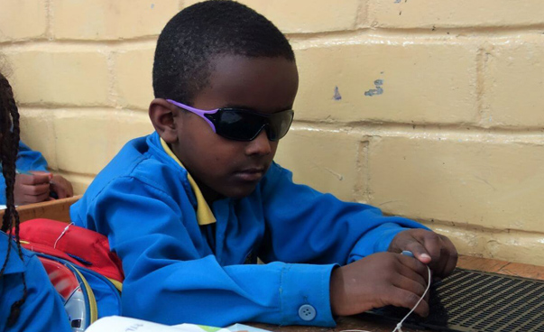 Ein kleiner sehbehinderter Junge arbeitet mit speziellem Material in der Schulbank.