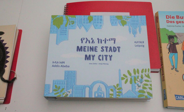 Das Kinderbuch „Meine Stadt Addis Abeba und Leipzig“ liegt auf einem Tisch. Das Cover ist blau-weiß gestaltet und zeigt Stadtelemente.