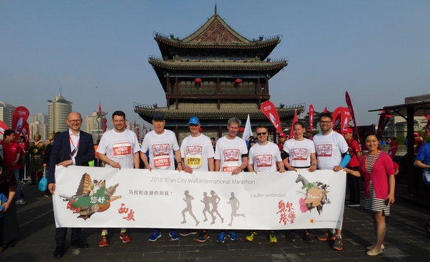 Zehn Sportlerinnen und Sportler halten ein Transparent. Im Hintergrund ein tempelartiges Bauwerk.