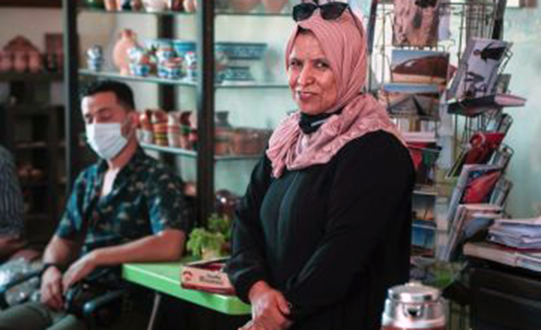 Video still: A woman in a store smiles at the camera; to her left is a man wearing a mouth guard.