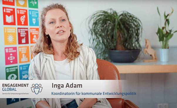 Die Koordinatorin für Kommunale Entwicklungspolitik Inga Adam sitzt vor einem Plakat mit den globalen Nachhaltigkeitssymbolen.
