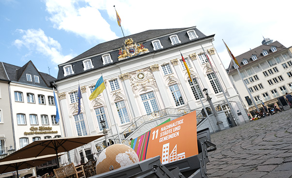 Blick auf das alte Bonner Rathaus; davor ein Globus sowie ein Schild mit dem Hinweis das SDG-Ziel 11: Nachhaltige Städte und Gemeinden