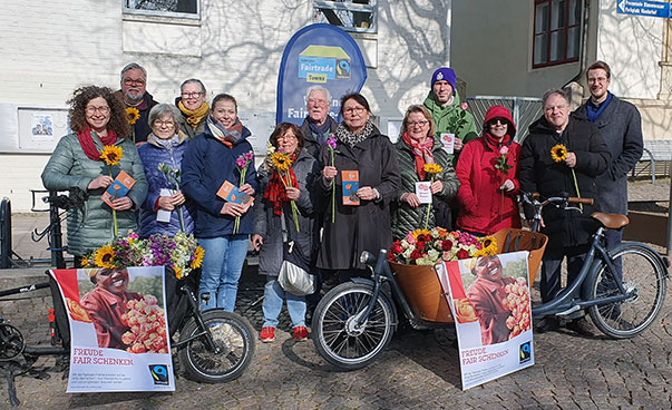Circa ein Dutzend Personen mit einer Sonnenblume in der Hand steht vor blumengeschmückten Fahrrädern.