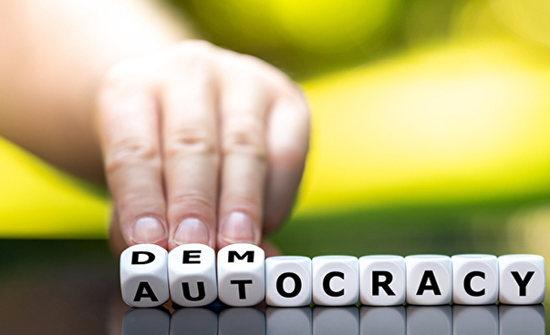 Eine Hand berührt einige weiße Würfel, deren Buchstaben zusammengenommen das Wort Democracy bilden.