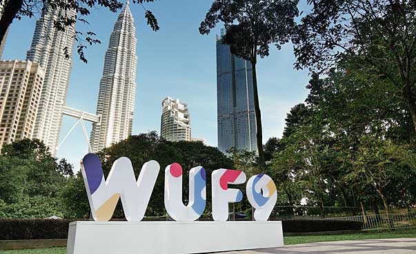 Blick auf die Buchstaben WUF und die Zahl neun, die das Akronym des neunten World Urban Forums sind, im Hintergrund befinden sind moderne Hochhäuser.