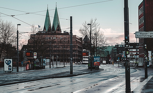 Stadtansicht von Bremen. Zu sehen sind eine leere Straße, im Hintergrund ein Parkhaus und zwei Kirchtürme. Foto:  Alex Plesovskich/Unsplash