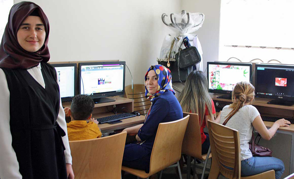 Blick in einen Computerraum. Eine Frau blickt im Vordergrund in die Kamera. Vier weitere Frauen sitzen vor den Computerbildschirmen.