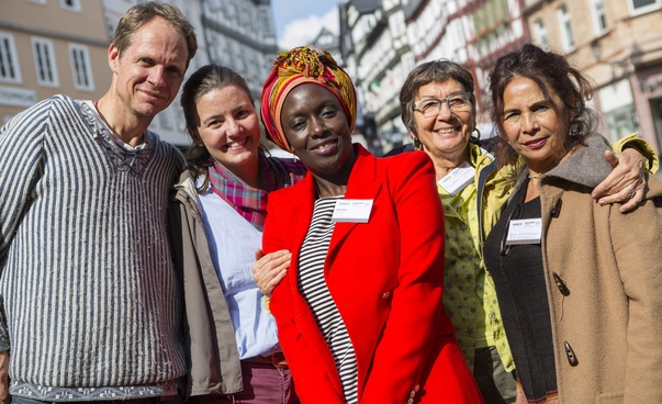 Ein Mann und vier Frauen im Halbporträt vor städtischer Kulisse lachen in die Kamera. Foto: Christian Lademann