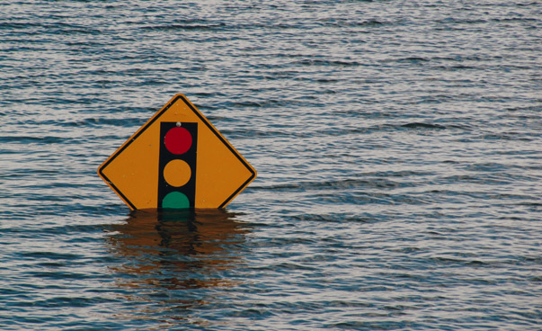 Ein Verkehrsschild mit einem Ampelsymbol steht mitten in einer Wasserflut.