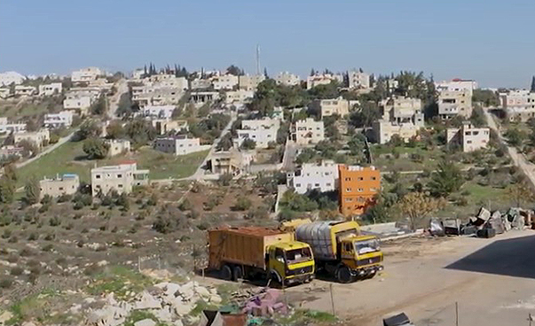 Screenshot aus dem Video über Jordanien. Zwei LKW stehen auf dem Gelände einer Kompostieranlage. Dahinter stehen Häuser am Hang.