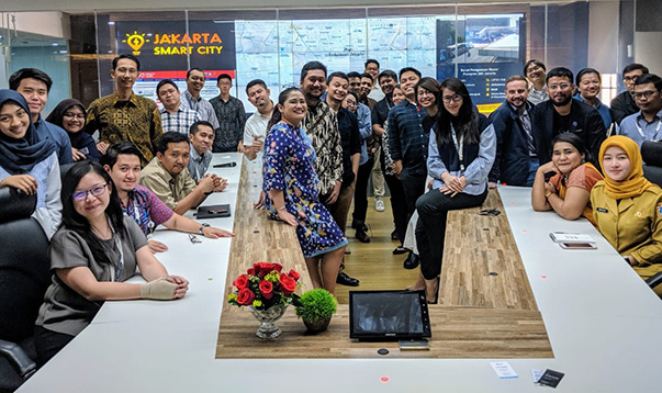Männer und Frauen gruppieren sich um einen hufeisenförmigen Tisch, im Hintergrund ist das Logo "Jakarta Smart City" zu sehen.
