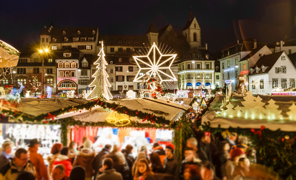 Weihnachtsmarktszene vor festlich beleuchteter Stadt.