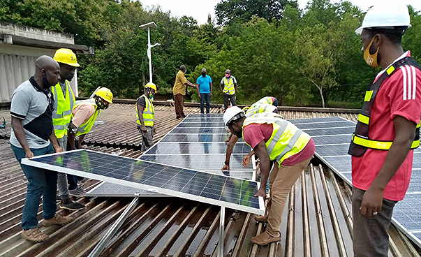 Männer mit Helmen und gelben Warnwesten bringen eine Photovoltaikanlage auf einem Dach an.