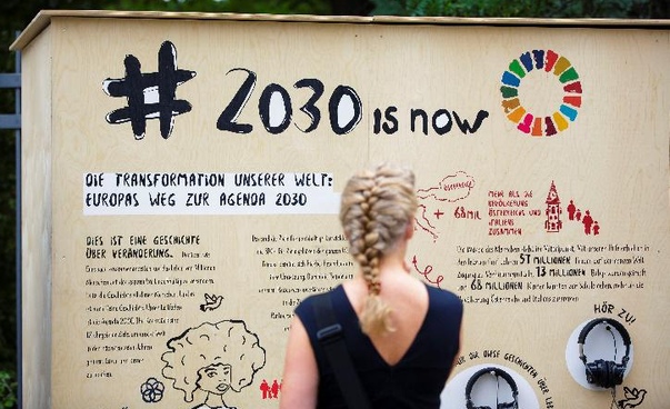 Eine Frau steht vor einer Wand, auf der auf die Agenda 2030 Bezug genommen wird.