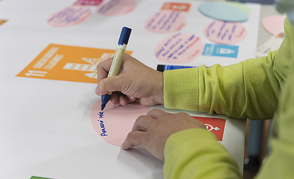 Eine Hand hält einen blauen Stift und schreibt etwas auf ein ovales rosa Post-it