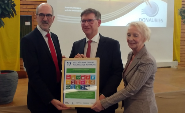 Dirk Schwenzfeier (BMZ), Landrat Stefan Rößle und Annette Turmann (SKEW) halten gemeinsam ein Plakat mit den Nachhaltigkeitssymbolen in die Kamera.