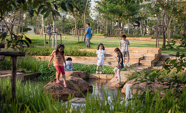 In einem schön angelegten Park spielen mehrere Kinder an einer Wasserstelle.