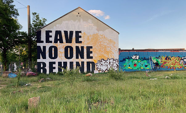 Auf der Fassade eines im Grünen stehenden Hauses steht in großer Schrift: Leave no one behind.