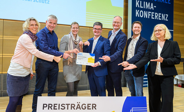 Sieben Personen im Wettbewerb „Klimaaktive Kommune“ lächeln als Preisträger in die Kamera.