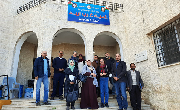 Eine Gruppe steht auf Stufen vor einem Gebäude; darüber ein blaues Schild in arabischer Schrift.