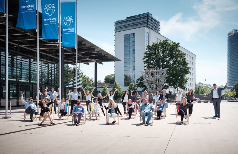 Die Mitarbeiter und Mitarbeiterinnen der Servicestelle Kommunen in der Einen Welt sitzen oder stehen mit Abstand zueinander vor dem Eingang des World Conference Center in Bonn und winken.