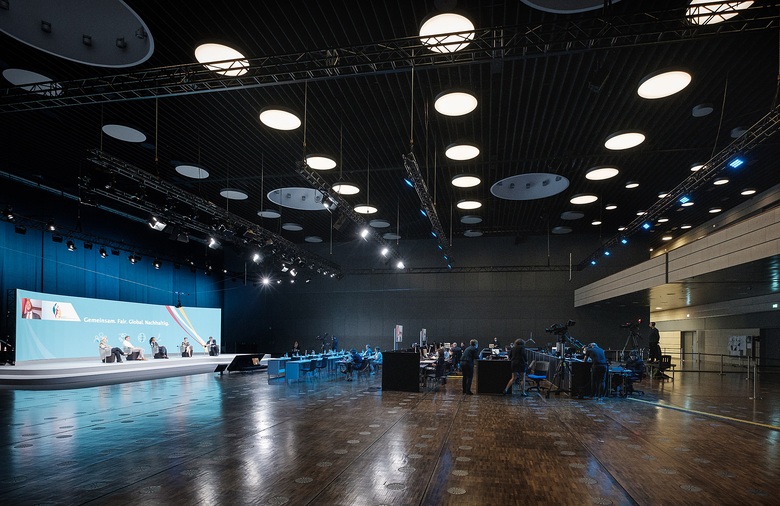 Blick in den Saal New York des World Conference Center Bonn mit Podiumsdiskussion auf der Bühne und Technikteam im Hintergrund.