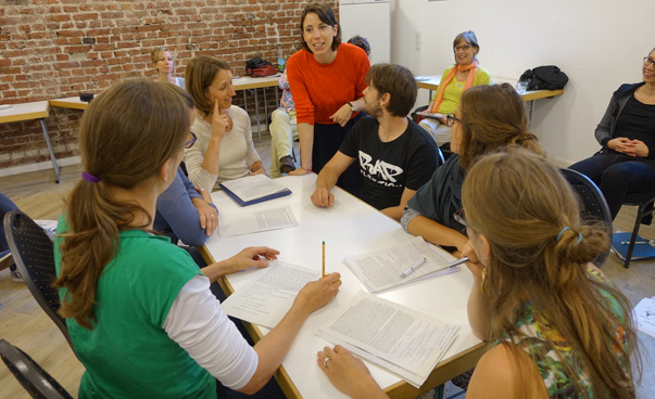 Eine Gruppe von Personen sitzt an einem Tisch, währen eine vor ihnen stehende Frau referiert. Foto: FEMNET e.V.