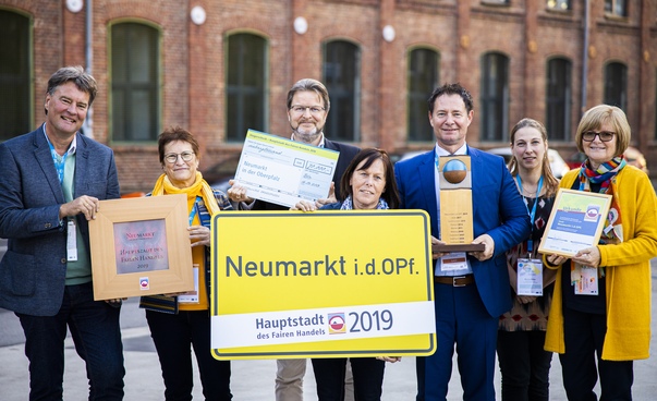 Vier Frauen und drei Männer halten Urkunden und ein gelbes Ortsschild von Neumarkt in die Kamera. Foto: Engagament Global