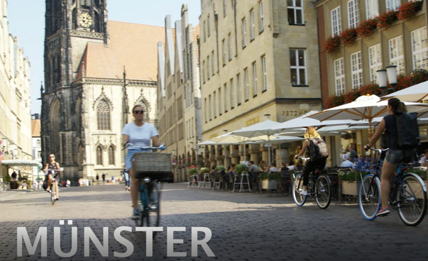 Eine historische Innenstadt mit Fahrradfahrern ist zu sehen; darunter der Schriftzug Münster.