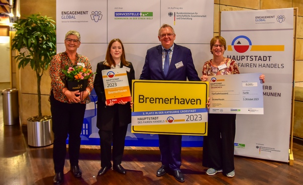 Die Delegation aus Bremerhaven mit Ortsschild, Urkunde und Scheck beim Wettbewerb Hauptstadt des Fairen Handels.