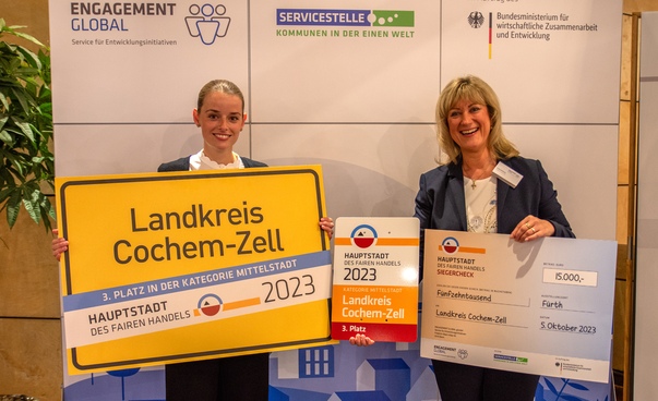 Zwei Frauen aus dem Landkreis Cochem-Zell mit Ortsschild, Urkunde und Scheck.