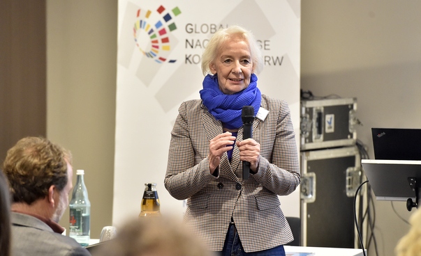 Annette Turmann von der Servicestelle Kommunen in der Einen Welt steht vor einem Banner mit dem Projekt Logo Global Nachhaltige Kommune Nordrhein-Westfalen