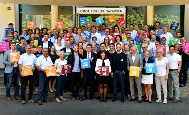 Gruppenfoto der Kommunalvertreterinnen und -vertreter aus Nordrhein-Westfalen. Die Personen halten bunte Schilder mit den globalen Nachhaltigkeitszielen in die Kamera.