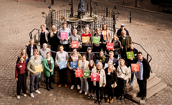 Die Teilnehmenden des Netzwerktreffens Global Nachhaltige Kommune Niedersachsen haben sich zum Gruppenbild aufgestellt. Sie halten Schilder mit den 17 Zielen in die Luft.