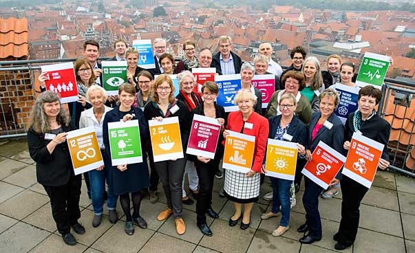 Eine Gruppe steht auf einem hohen Gebäude, einige der Personen halten Symbole der 17 nachhaltige Entiwicklungsziele. Foto: 2017 H.-J.Wege