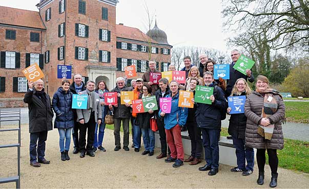 Eine Gruppe steht vor einem historischen Gebäude, die Personen halten Schilder mit den Symbolen der 17 nachhaltigen Entwicklungsziele in Händen.