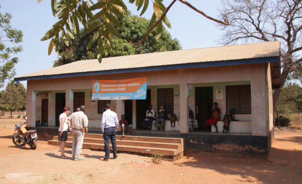 Eine kleine Gruppe von Männern, Frauen und Kindern vor einem Haus, einer Gesundheitsstation in Masasi.