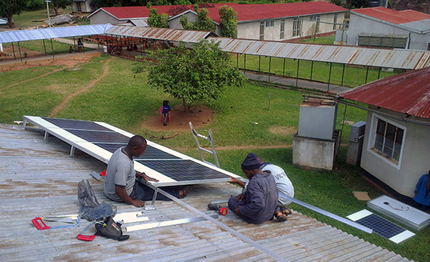 Três pessoas a trabalhar num módulo solar sobre um telhado.